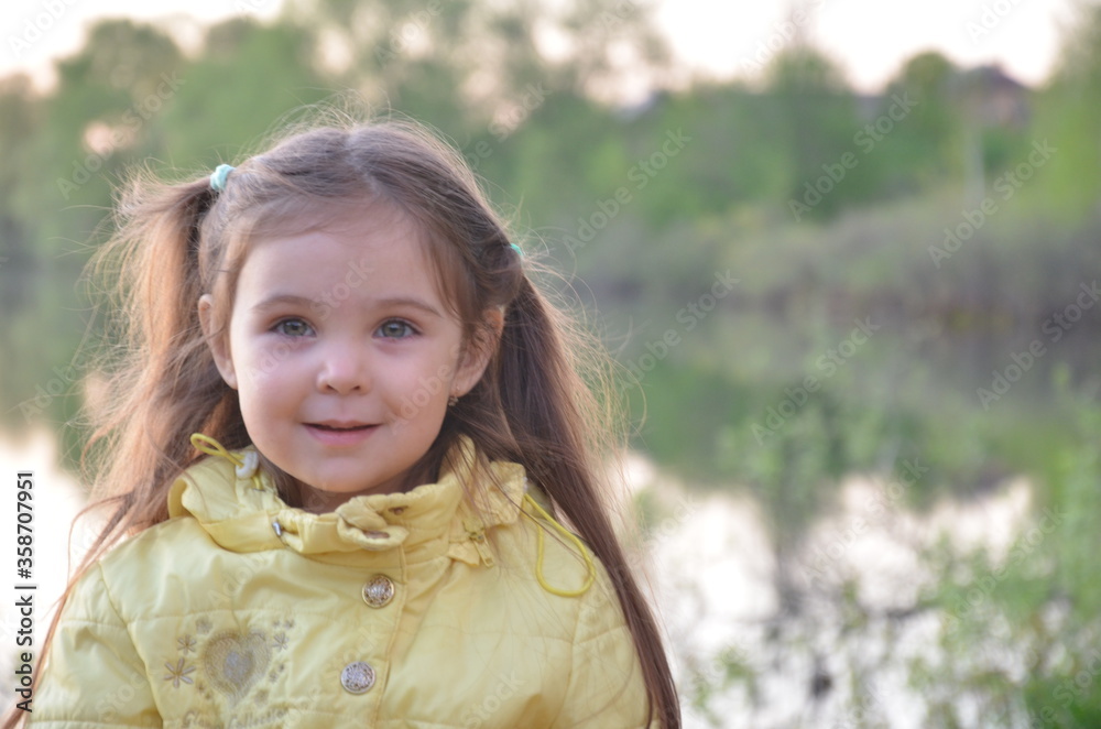 a little girl in an autumn or spring jacket stands near the lake, smiles. A tourist by a small lake with a deep blue bottom. The nature a little girl in an autumn or spring jacket stands near the lake, smiles. A tourist by a small lake with a deep blue bottom. The nature