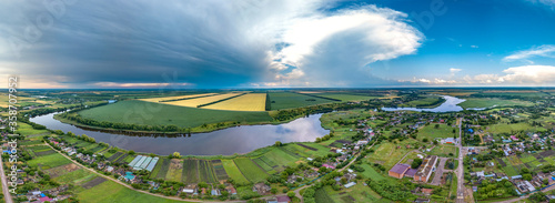 Bratsky farm in the south of Russia, surrounded by fields near a flat river with a dam - little aerial panorama with a sunny and rainy day