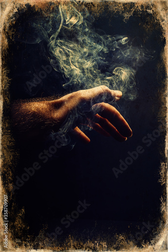 hand in smoke on black background. Old photo effect.