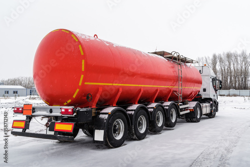 Oil tanker truck with a red tank semi-trailer. The picture was taken in Russia, in winter in snowfall