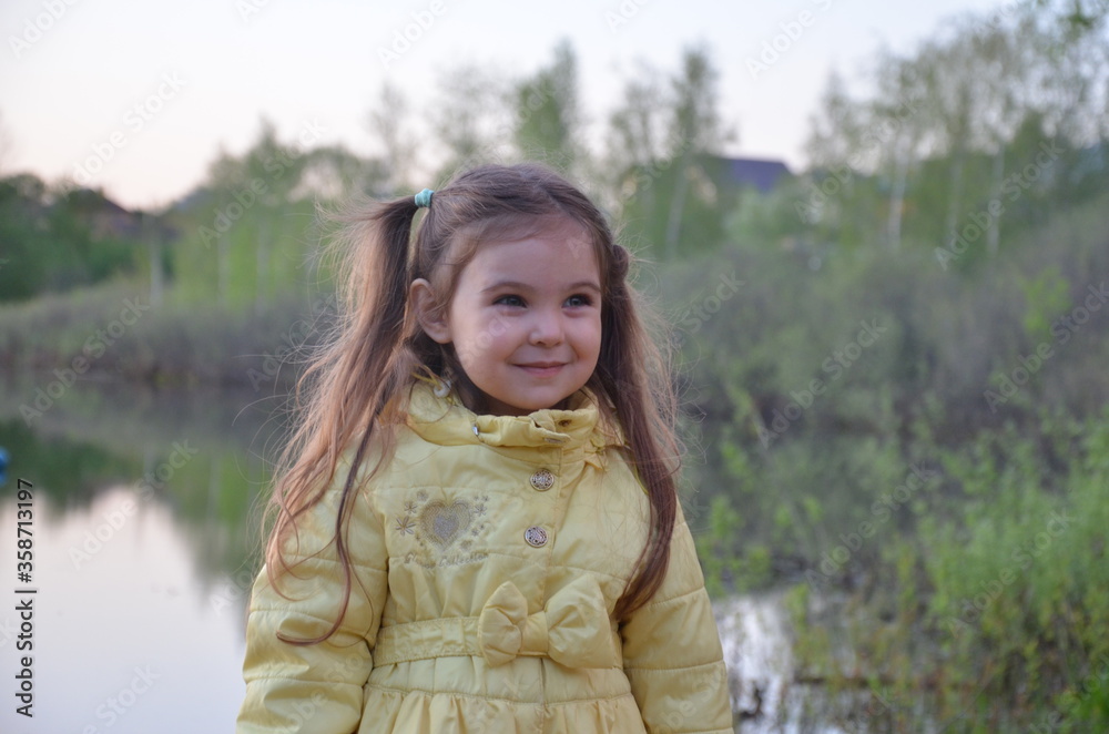 a little girl in an autumn or spring jacket stands near the lake, smiles. A tourist by a small lake with a deep blue bottom. The nature a little girl in an autumn or spring jacket stands near the lake, smiles. A tourist by a small lake with a deep blue bottom. The nature