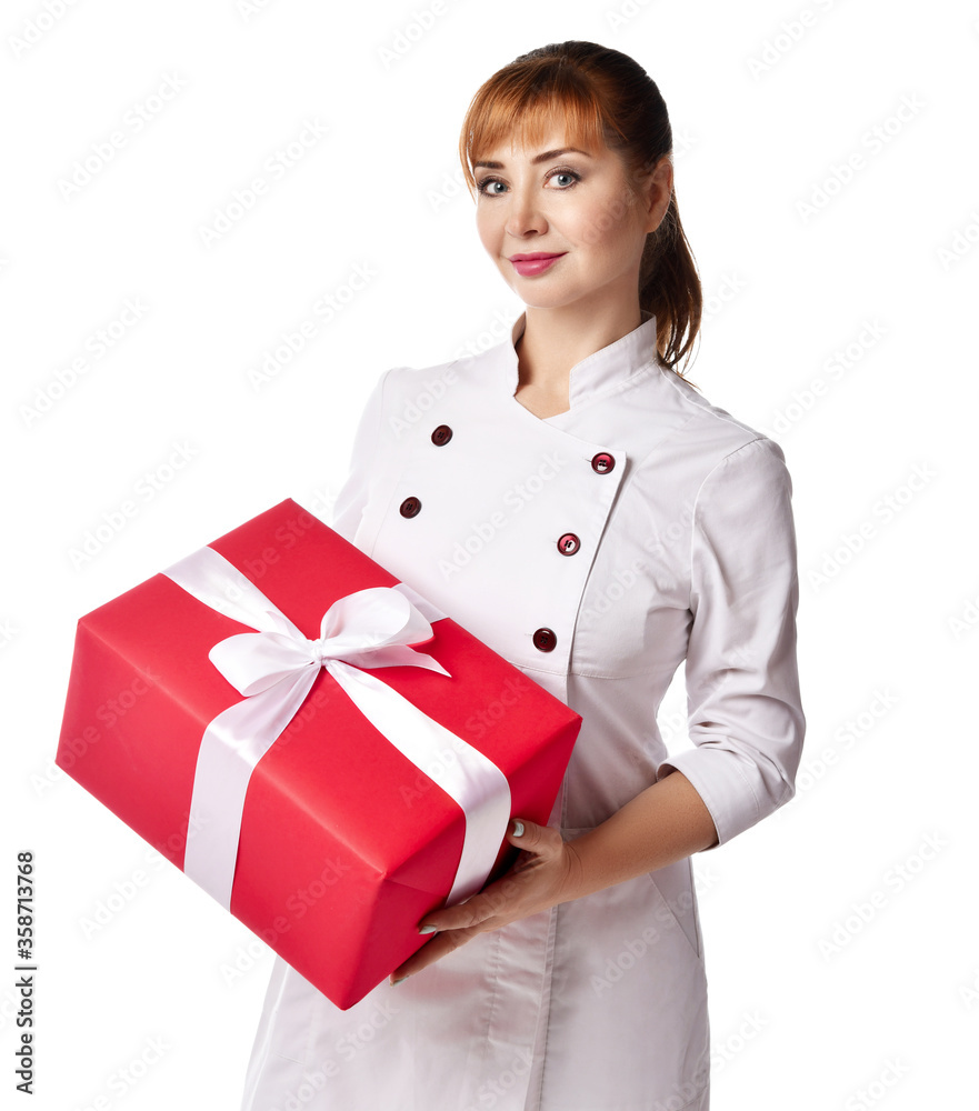Portrait of young beautiful red-haired woman doctor or nurse in white medical uniform standing holding big present box with ribbon Portrait of young beautiful red-haired woman doctor or nurse in white medical uniform standing holding big present box with ribbon