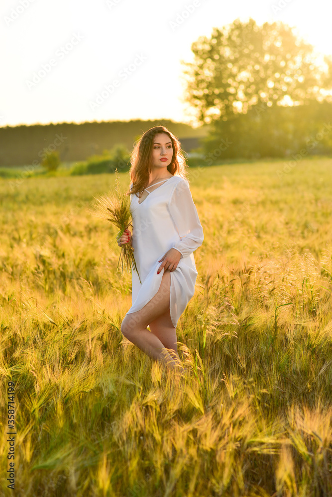 Beautiful young woman wearing white dress in wheat field relaxing. Glow sun Beautiful young woman wearing white dress in wheat field relaxing. Glow sun