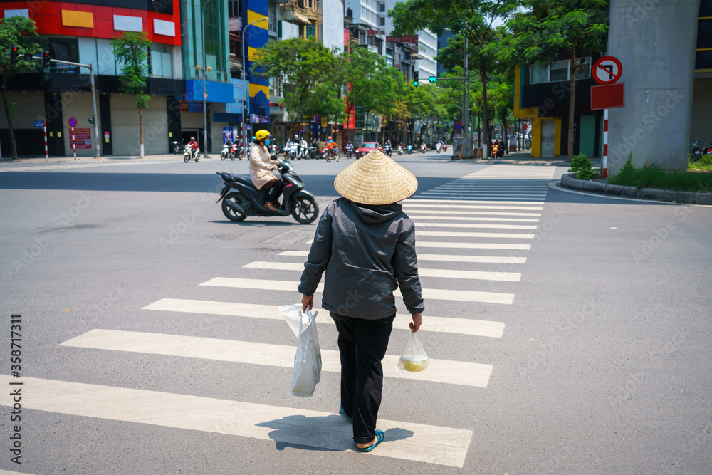 Vietnamese woman with conical hat walking on crosswalk in Hanoi