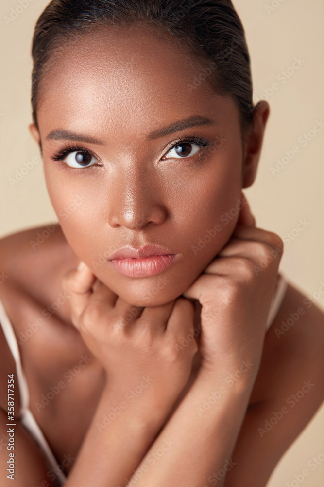 Woman. Ethnic Model Beauty Portrait. Beautiful Mixed Race Female With Hands Under Chin Looking At Camera. Charming Girl With Perfect Skin And Nude Makeup On Beige Background. Woman. Ethnic Model Beauty Portrait. Beautiful Mixed Race Female With Hands Under Chin Looking At Camera. Charming Girl With Perfect Skin And Nude Makeup On Beige Background.