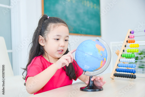 Pretty asian girl looking and pointing at a globe at school.Child education concept.