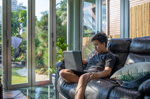Asian boy uses laptop for studying from home with garden view background
