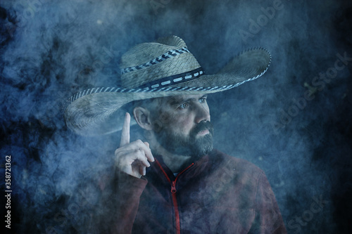 farmer hipster in a straw hat with brim in smoke smoking tobacco retro style wild west sambrero photo