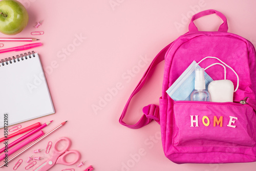 Studying at home concept. Top above overhead flat lay view photo of pink backpack with mask, sanitizer and soap and pink stationery isolated on pastel pink background with copyspace