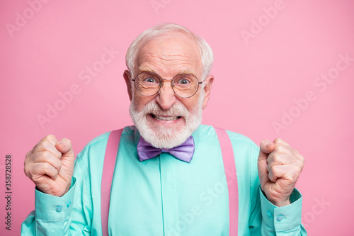 Closeup photo of crazy grandpa negative facial expression grimace outraged raise fists grinning wear specs mint shirt suspenders violet bow tie isolated pink pastel color background