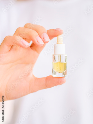 Dropper jar with cosmetic oil. Close up vertical shot female hand holds a bottle without a label