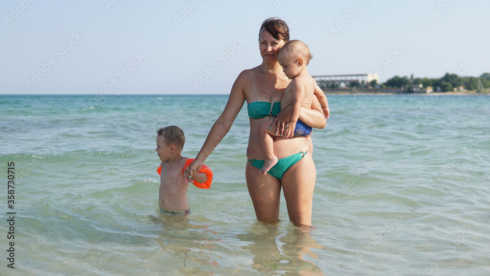 Young mother standing in water in sea with two little boys Young mother standing in water in sea with two little boys