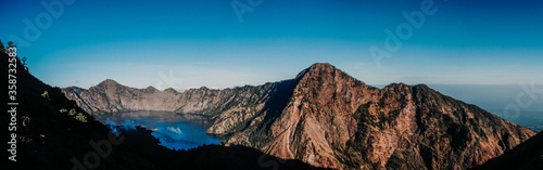 Panorama view of Segara Anak Lake in Mount Rinjani, Lombok, Indonesia. Sunny afternoon. wonderful springtime landscape in mountains. grassy field and rolling hills. rural scenery