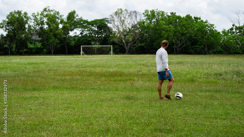 young attractive man training with soccer ball on soccer green field background