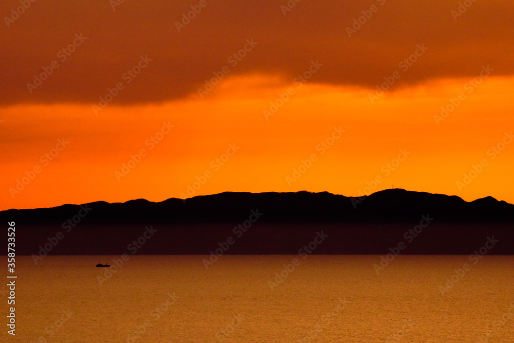 海に浮かぶ小舟とシルエットの山と夕日