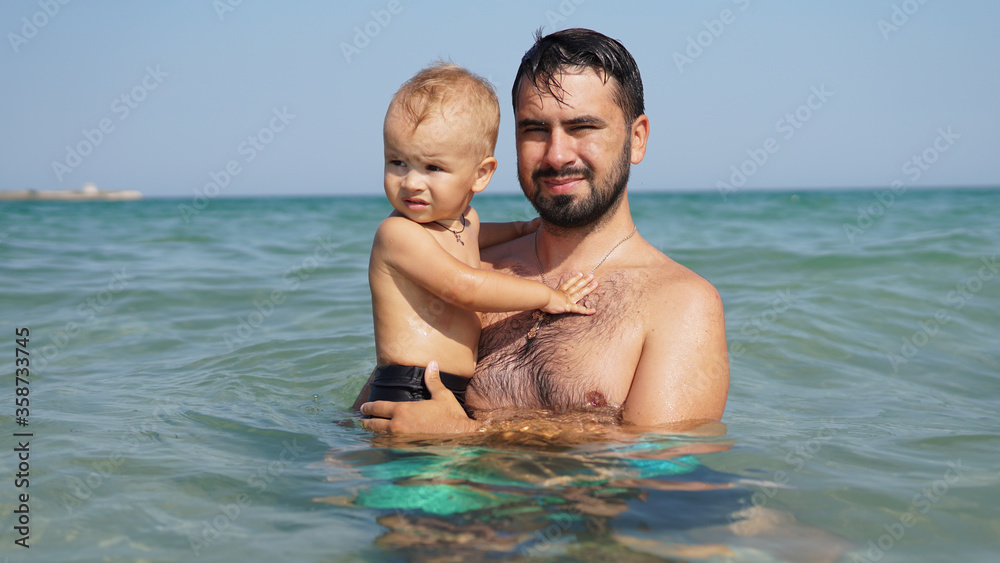 Little happy kid and his smiling father in sea. Dad holding boy Little happy kid and his smiling father in sea. Dad holding boy