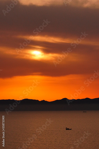 海に浮かぶ小舟とシルエットの山と夕日
