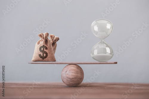 Financial concept : Write sand clock or hourglass symbol and dollar bagson a balance scale in equal position.Time value of money, asset growth over time, investment in long-term equity for more money  photo