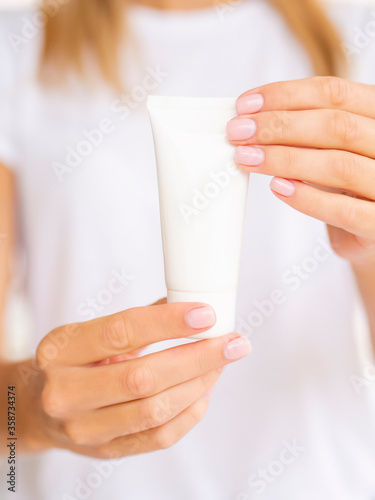 beautiful female hands show a white clean tube of cream. Mockup with copy space for logo. Vertical front view