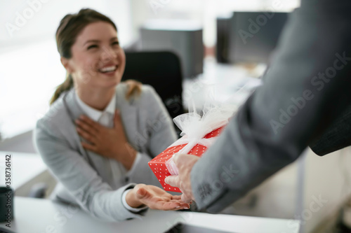 Young businessman giving his colleague present in office. Young man suprise beautiful businesswoman in office.	
