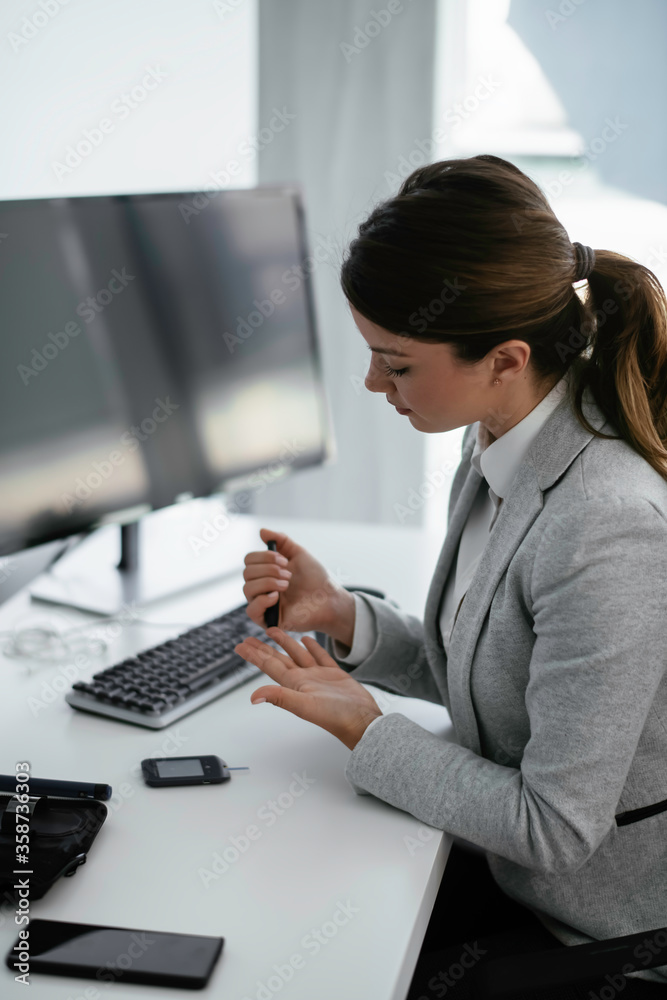 Beautiful businesswoman using lancet pen in office. Young woman checking blood sugar level	