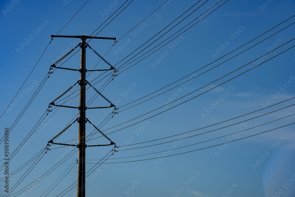 Kuching, Sarawak / Malaysia - August 28, 2017: Power pole and cables silhouetted in blue sky. Kuching, Sarawak / Malaysia - August 28, 2017: Power pole and cables silhouetted in blue sky.
