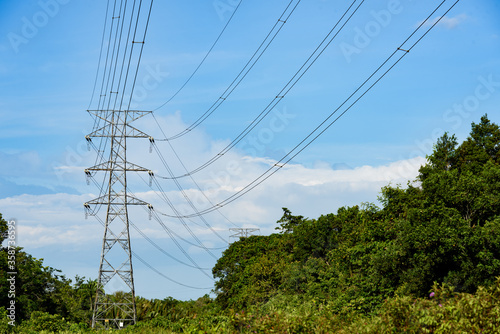 Kuching, Sarawak / Malaysia - August 28, 2017: Power pole and cables erected across bushes and tress in blue sky.
