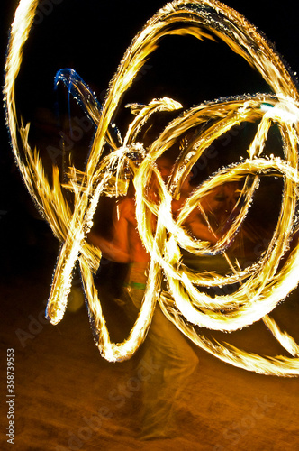 Long exposure shot from a fire juggling act, performed by a man with a red hat, showing the light trail create by the 3 burning torches.