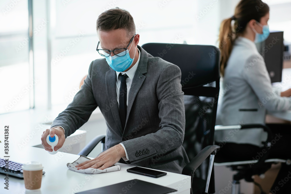 Handsome businessman disinfecting desk in the office.	