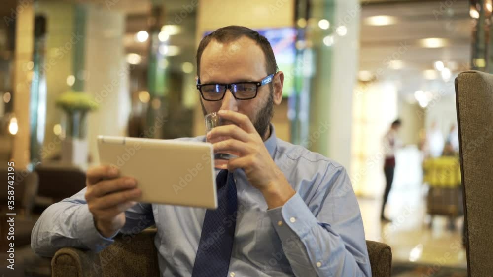 Young, happy businessman watching movie on tablet in hotel lobby Young, happy businessman watching movie on tablet in hotel lobby