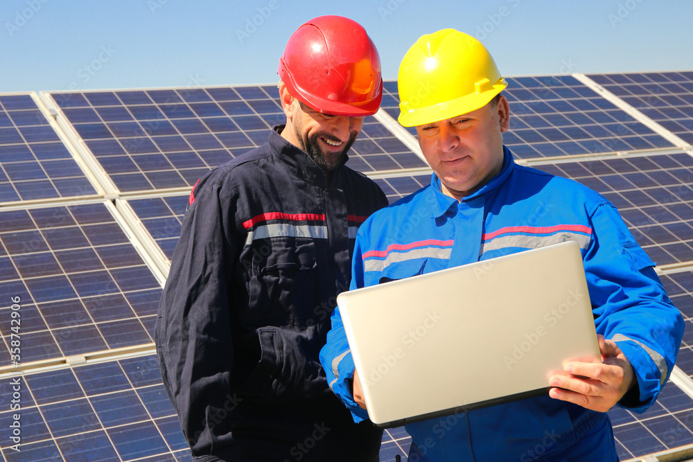 Green energy, solar collectors and two electricians with laptop Green energy, solar collectors and two electricians with laptop