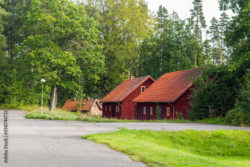 Old traditional red wooden cozy swedish summerhouse in the nature near the forest with many green trees and grass