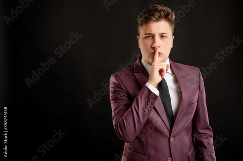 Law student with blond hair dressed in burgundy jacket, white shirt and black tie showing shh gesture