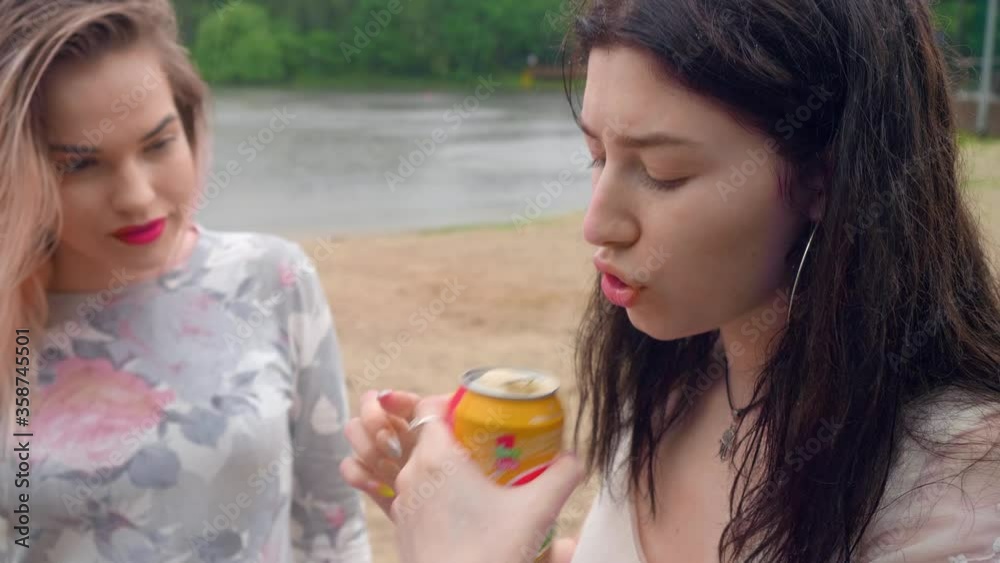 Brunette tries to open a can of beer, blond girl is watching. Afternoon of youngsters. Brunette tries to open a can of beer, blond girl is watching. Afternoon of youngsters.