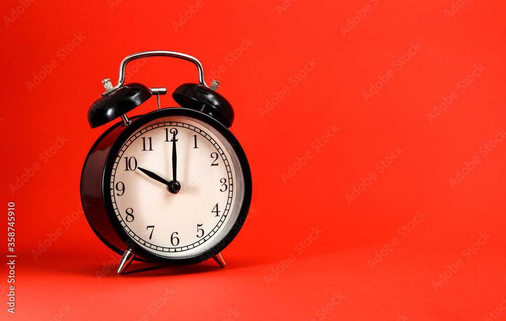 An old alarm clock showing 10 o'clock on red background An old alarm clock showing 10 o'clock on red background