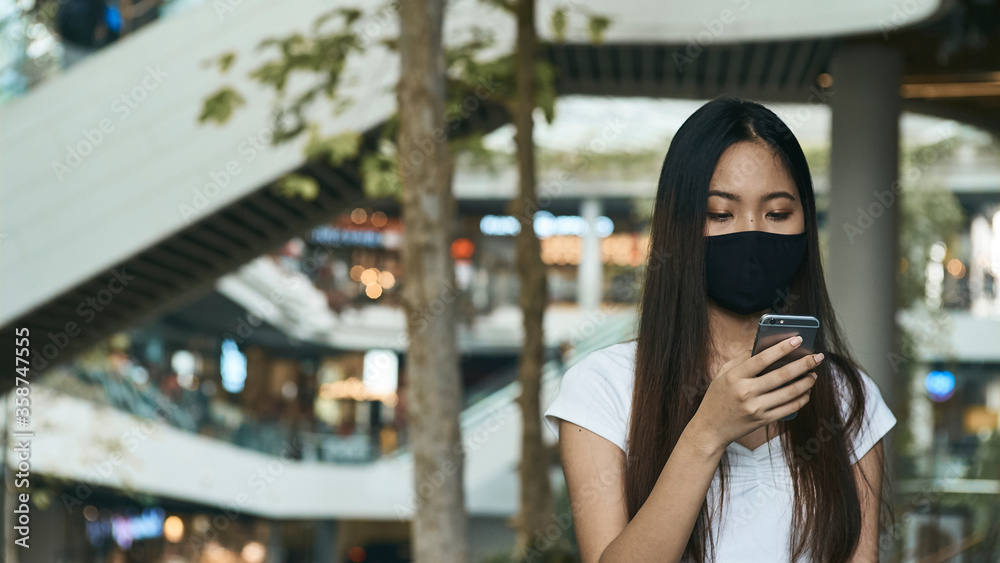 Woman wearing a mask and using a smartphone for business, social media, working and waiting for someone in the public. Woman wearing a mask and using a smartphone for business, social media, working and waiting for someone in the public.