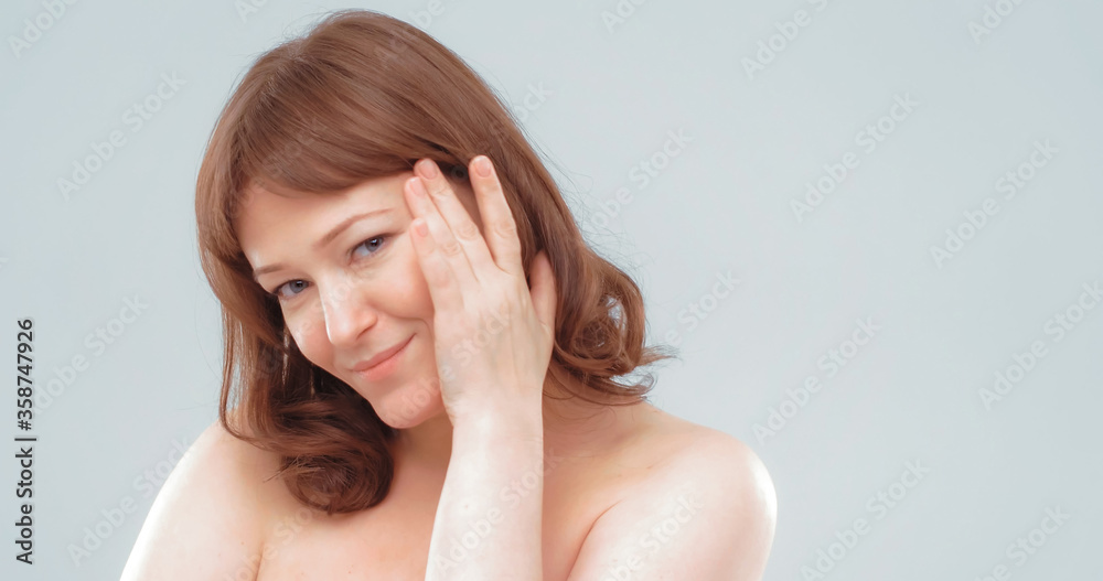 Naked smiling mature woman touches face with hand applying skin care product. Anti-aging skin care concept. Empty space for text at right side. Naked smiling mature woman touches face with hand applying skin care product. Anti-aging skin care concept. Empty space for text at right side.