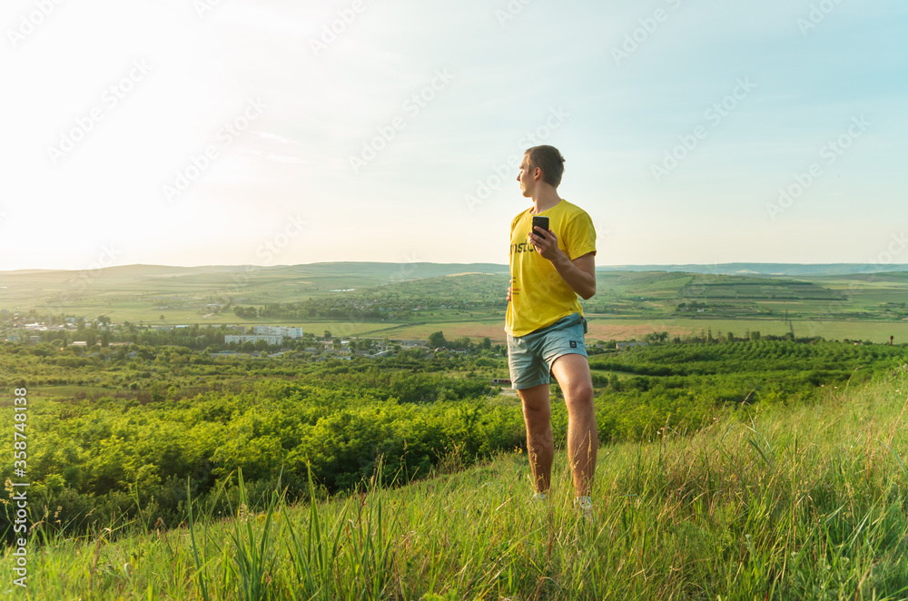Young man with cellphone  standing on a hill looking over rural landscape