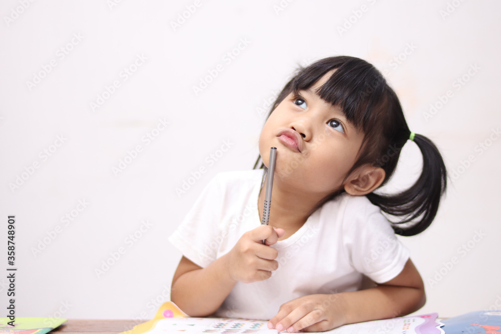 Cute litle Asian baby girl holding pen and book, studying and learning while thinking something or having good idea, smiling and looking up, imagination Cute litle Asian baby girl holding pen and book, studying and learning while thinking something or having good idea, smiling and looking up, imagination