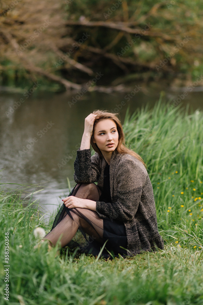 Stylish model girl in clothes on the grass near the small river reeds trees Stylish model girl in clothes on the grass near the small river reeds trees