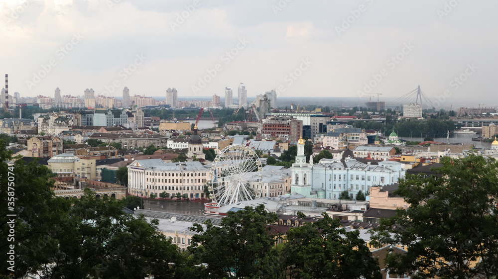The view from the height of the Podolsky district of the city of Kiev, the old square with a Ferris wheel and a bell tower with a gilded dome. Beautiful cityscape in the summer.