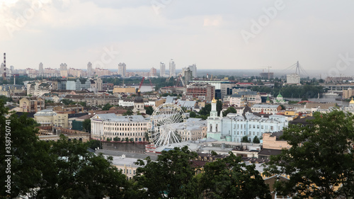 The view from the height of the Podolsky district of the city of Kiev  the old square with a Ferris wheel and a bell tower with a gilded dome. Beautiful cityscape in the summer.