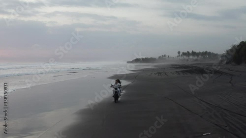 Drone aerial of couple on motorcyle at blacks sand pasut beach in Bali Indonesia photo
