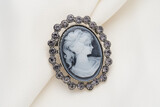 Cameo brooch, which is a side portrait of a woman, with small crystals around the edges on a white background.