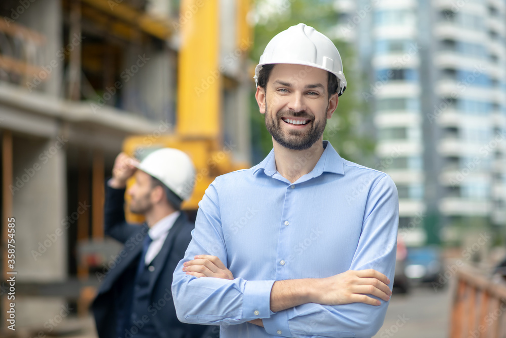 Foreman standing with folded arms, building supervisor standing behind him, looking at the building Foreman standing with folded arms, building supervisor standing behind him, looking at the building