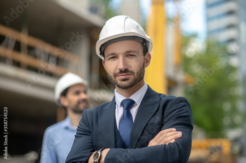 Building supervisor standing with folded arms, foreman looking sideways behind him