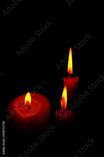 Three red candles burn with a bright flame. Vertical frame. Black background.