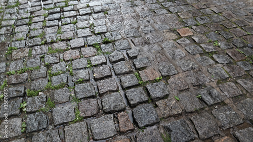 A wet sidewalk creates a shiny backdrop. Beautiful gray stone background. Stone road, paving stones in the old town during the rain during the daytime.