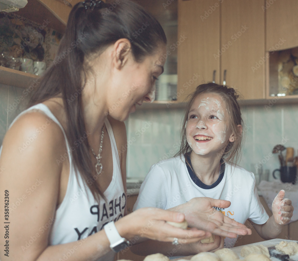 Daughter and mother sit in the kitchen at the table and cook from the dough. A woman teaches a girl to cook deliciously. They have fun and joyful time with each other. High quality photo Daughter and mother sit in the kitchen at the table and cook from the dough. A woman teaches a girl to cook deliciously. They have fun and joyful time with each other. High quality photo