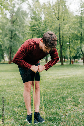 Young sportsman pulling up resistance band on lawn in park